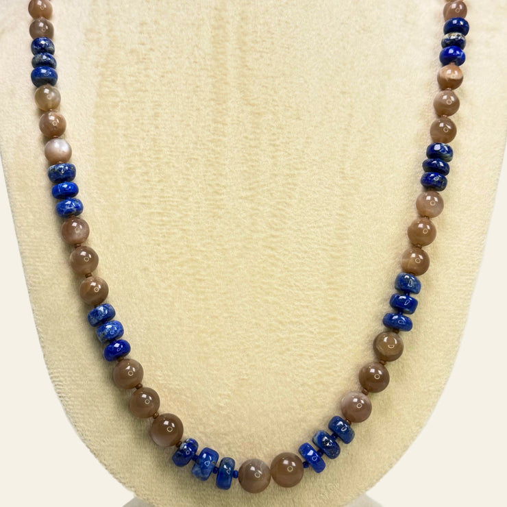 Necklace with brown and blue beads on a beige display stand