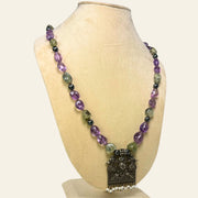 Necklace with purple and green beads on a mannequin bust against a white background