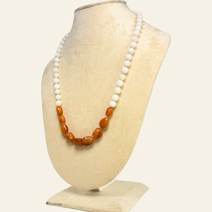 Necklace with white and amber beads on a beige mannequin bust.