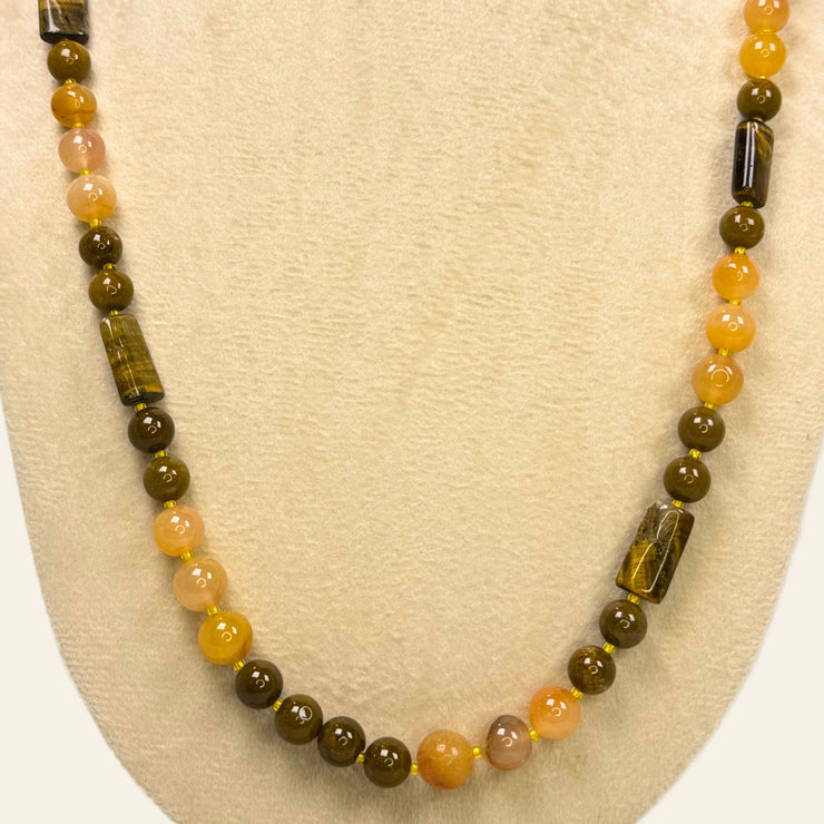 Beaded necklace with brown, orange, and green beads on a beige display stand.