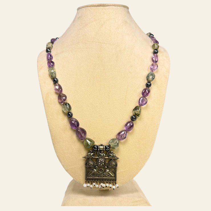 Necklace with multicolored beads and an ornate pendant on a beige stand.